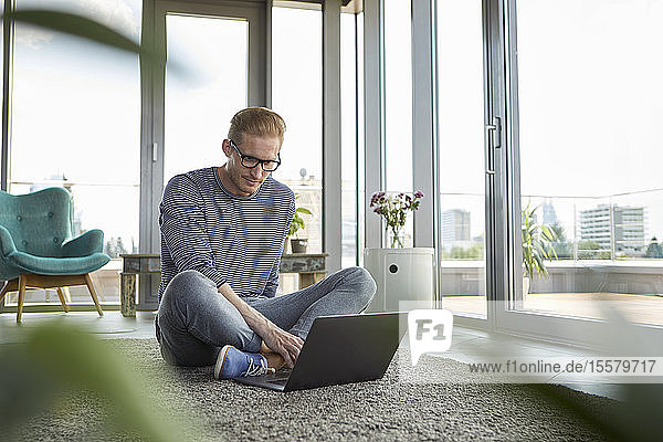 Young man sitting on carpet at home using laptop