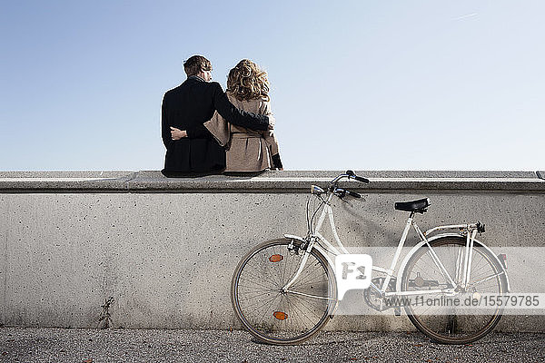 Germany  Bavaria  Munich  Young couple sitting on wall with bike
