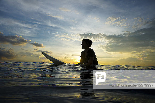 Indonesien  Bali  Canggu  Silhouette einer jungen Frau mit Surfbrett in der Dämmerung
