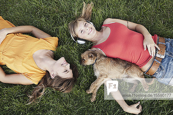 Germany  Cologne  Young woman lying in grass with dog  smiling