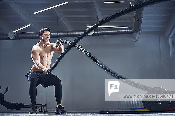 Athletic man exercising with battle ropes at gym