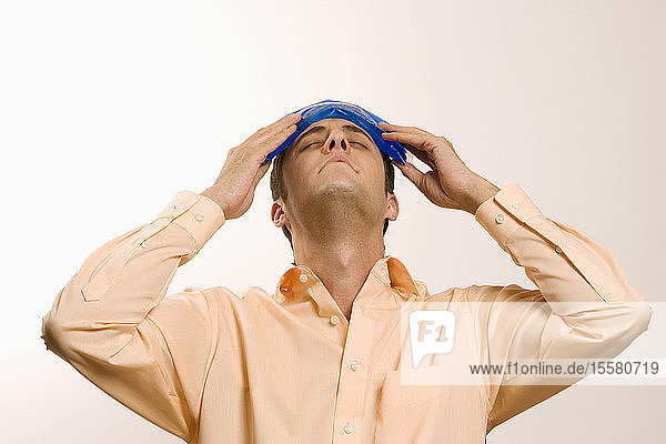 Young man holding ice pack on head  eyes closed