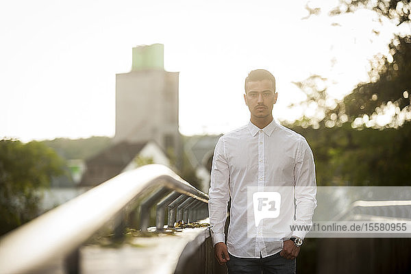 Serious looking young man wearing white shirt standing at backlight