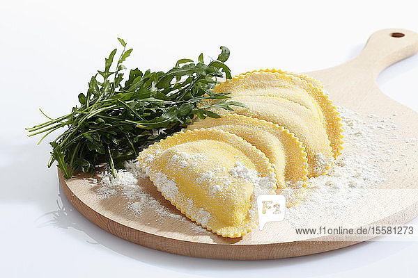 Halbmondförmige Teigwaren mit Mehl und Rucola auf Schneidebrett