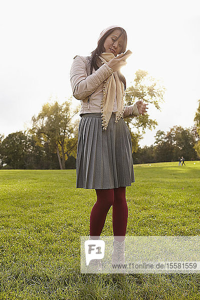 Deutschland  Köln  Junge Frau mit Handy im Park