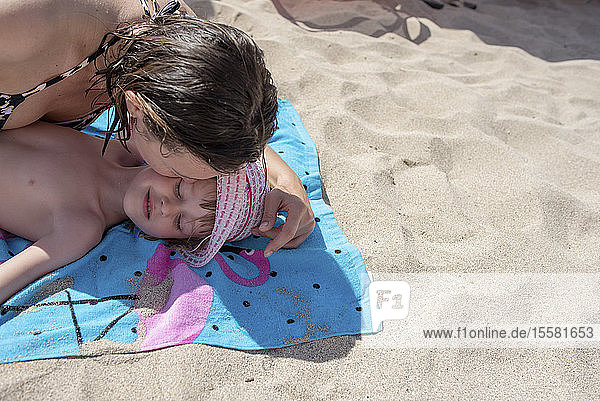 Mutter küsst Tochter  die auf einem Strandtuch am Strand liegt