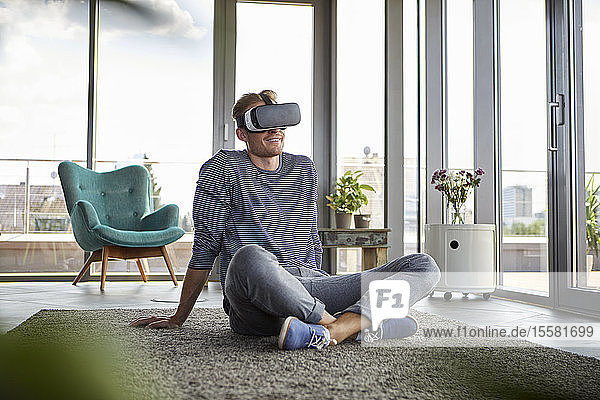 Junger Mann sitzt zu Hause auf Teppich mit VR-Brille