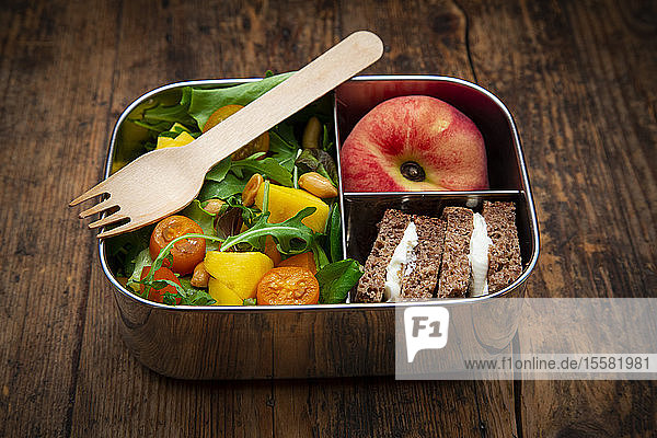 Nahaufnahme von gesundem Salat mit Sandwiches und Obst in Lunchbox auf dem Tisch
