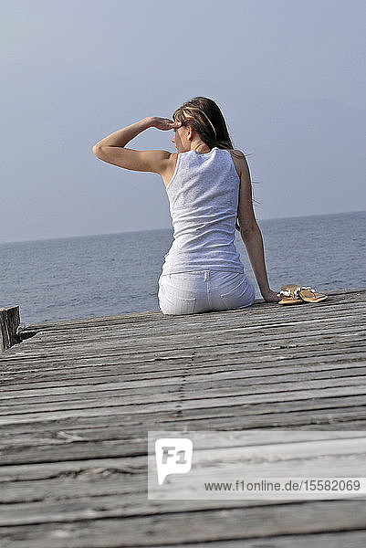 Italien  Gardasee  Junge Frau (20-25) auf dem Dock sitzend  Rückansicht  Nahaufnahme