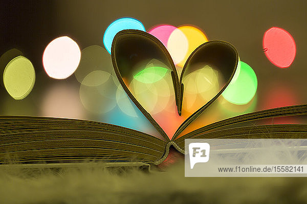 Herzförmige Buchseiten vor bunten Lichtern