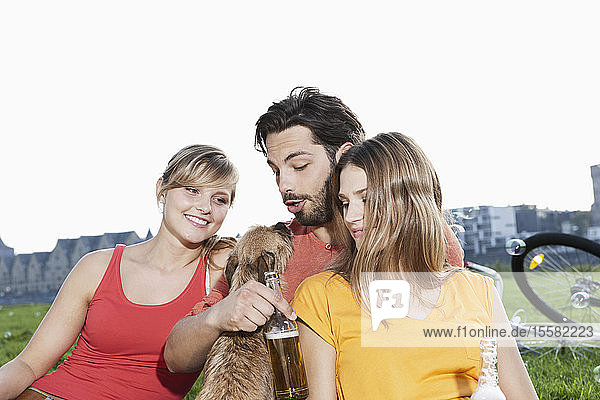 Germany  Cologne  Young man and woman with dog and beer bottle in grass  smiling