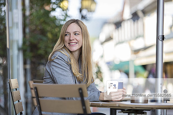 Lächelnde junge Frauen sitzen im Straßencafé mit Kaffee zum Mitnehmen