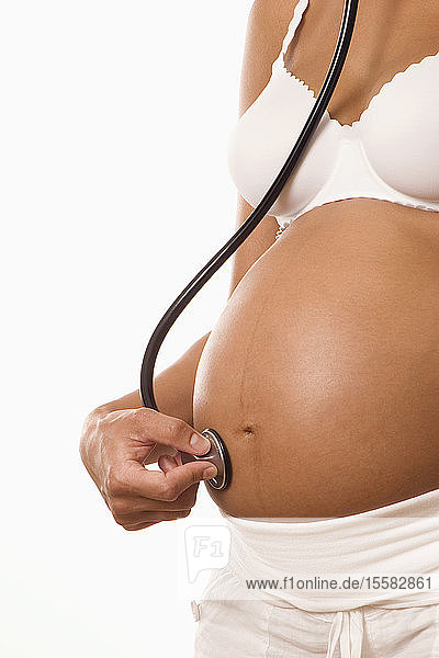 Schwangere Frau hält Stethoskop am Körper  Mittelteil