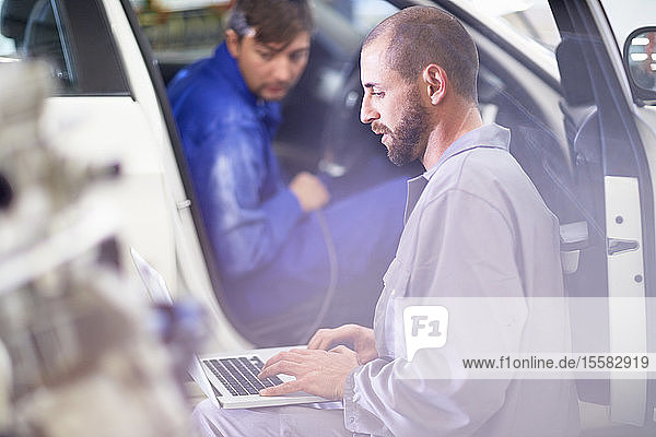 Zwei Automechaniker mit Laptop in Reparaturwerkstatt