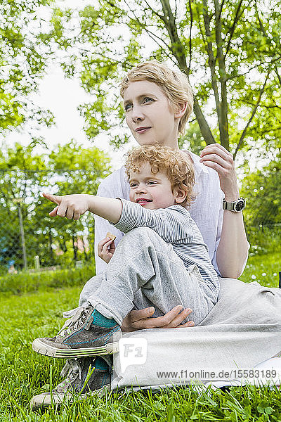 Mutter und kleiner Sohn sitzen zusammen auf einer Wiese und beobachten etwas