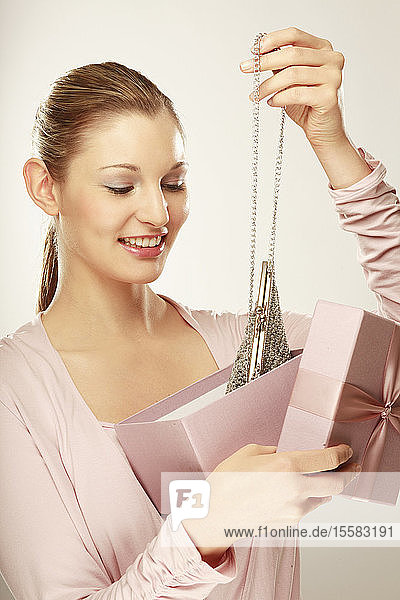 Junge Frau hält Geschenkkarton mit Handtasche in der Hand und lächelt