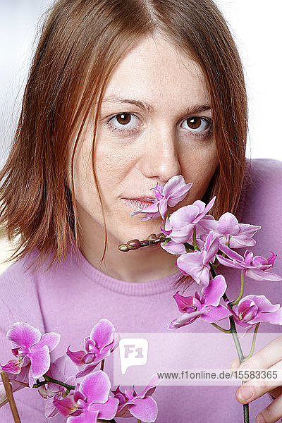 Junge Frau riecht Orchidee  Porträt  Nahaufnahme