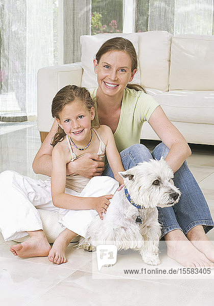 Germany  Mother and daughter sitting with dog near sofa