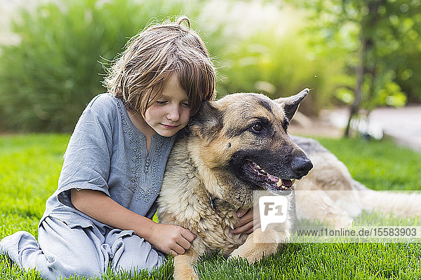 5 Jahre alter Junge spielt mit seinem Deutschen Schäferhund auf grünem Rasen