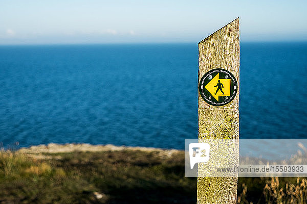 Steinwegweiser auf dem Pembrokeshire Coast Path National Trail  mit dem Ozean im Hintergrund.