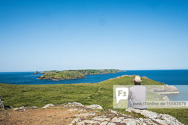 Rückansicht eines Mannes  der auf einer Klippe mit Blick auf die Küste von Pembrokeshire  Wales  Großbritannien  sitzt.