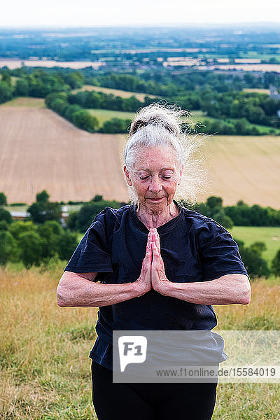 Ältere Frau  die an einem Yogakurs an einem Berghang teilnimmt.