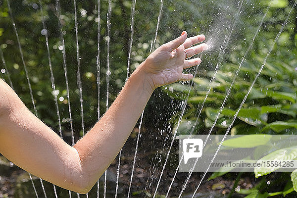 Die Hand einer Frau berührt den Sprühstrahl eines Sprinklers