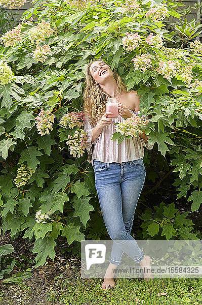 Lächelnde junge Frau mit Smoothie in der Hand und Blumen