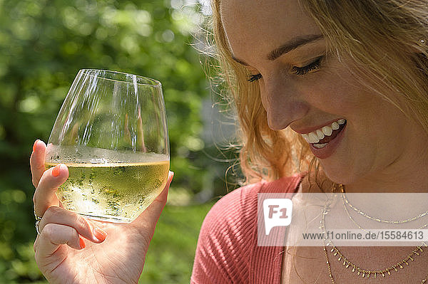 Lächelnde junge Frau hält ein Glas Weißwein