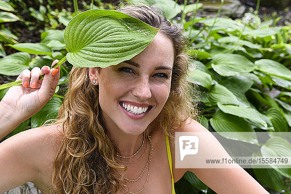Smiling young woman holding green leaf