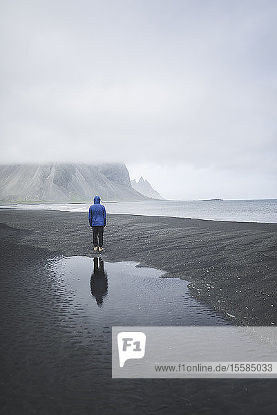 Mann mit blauem Mantel am schwarzen Sandstrand in KirkjubÂµjarklaustur  Island