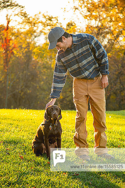 Mann streichelt schokoladenfarbenen Labrador auf einem Feld im Herbst