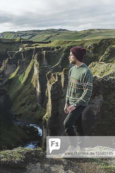 Young man standing on cliff above canyon in KirkjubÂµjarklaustur  Iceland