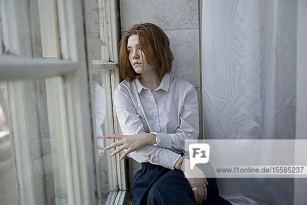 Junge Frau mit weißem Hemd auf dem Fensterbrett