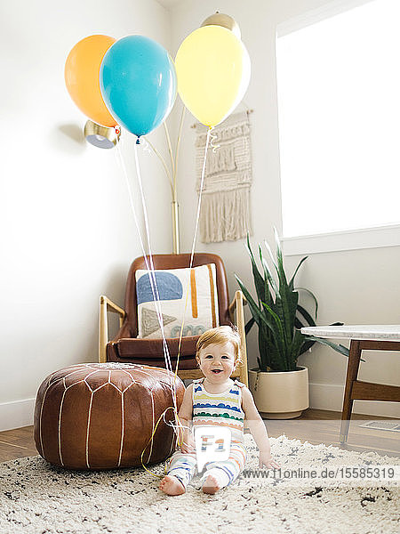 Kleiner Junge hält Luftballons im Wohnzimmer