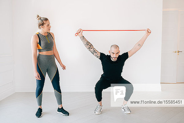 Woman observing fitness instructor using resistance band in studio