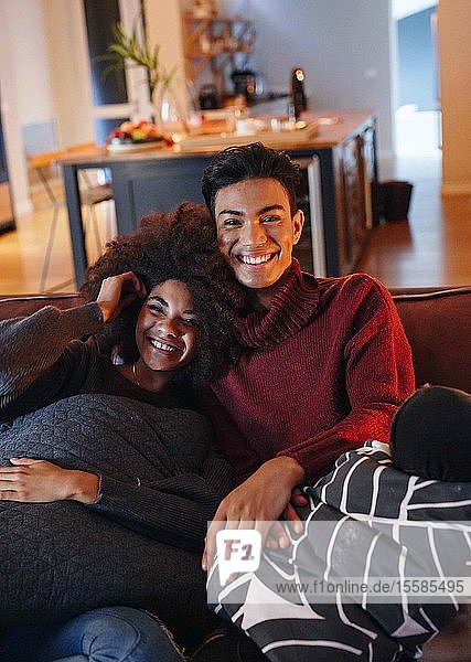 Junger Mann und junge Freundin lächeln beim Fernsehen auf dem Wohnzimmersofa