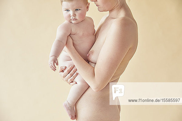 Naked mother carrying naked baby in arms
