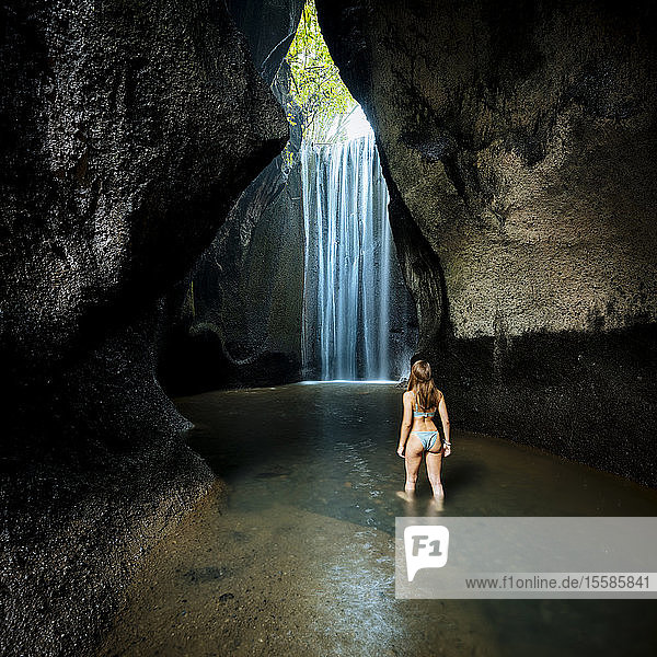 Junge Touristin im Bikini mit Blick auf Felsformation Wasserfall  Rückansicht  Bali  Indonesien