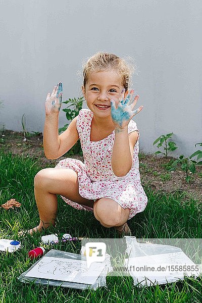 Fröhliches kleines Mädchen spielt mit Farbe im Garten