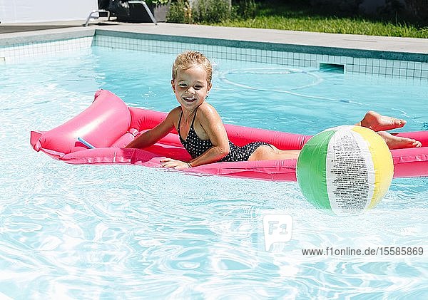 Glückliches kleines Mädchen liegt auf einer aufblasbaren Liege im Schwimmbad
