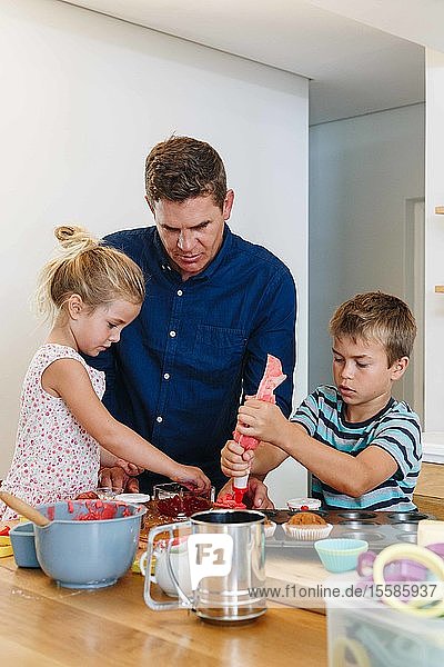 Vater und Kinder dekorieren Törtchen mit Zuckerguss in der Küche