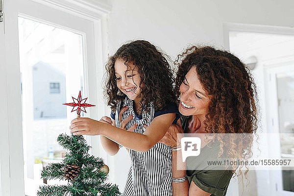 Mutter hilft Tochter  zu Hause einen Stern auf den Weihnachtsbaum zu setzen
