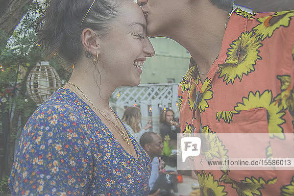 Junger Mann gibt seiner Freundin auf der Gartenparty einen Kuss auf die Stirn  Seitenansicht beschnitten