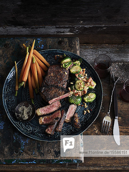 Rustic low key still life with plate of rubbed steak and spiced brussels sprouts on table overhead view