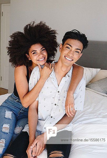 Happy young woman with arms around boyfriend while sitting on bed  portrait