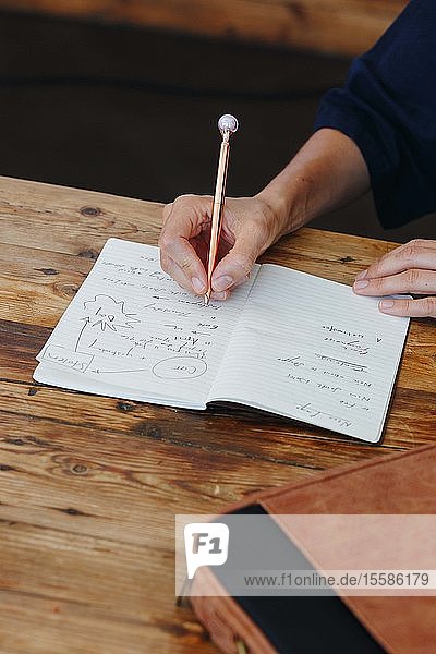 Frau schreibt in Notizbuch auf Tischplatte