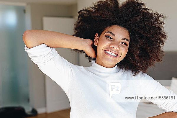 Glückliche junge Frau mit Hand in Afrohaar im Schlafzimmer  Kopf- und Schulterporträt