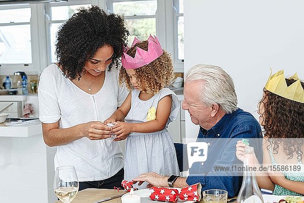 Frau unterrichtet Tochter Tochter faltet Papierblume am Esstisch