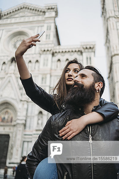 Couple playing piggyback ride and taking selfie  Santa Maria del Fiore  Firenze  Toscana  Italy